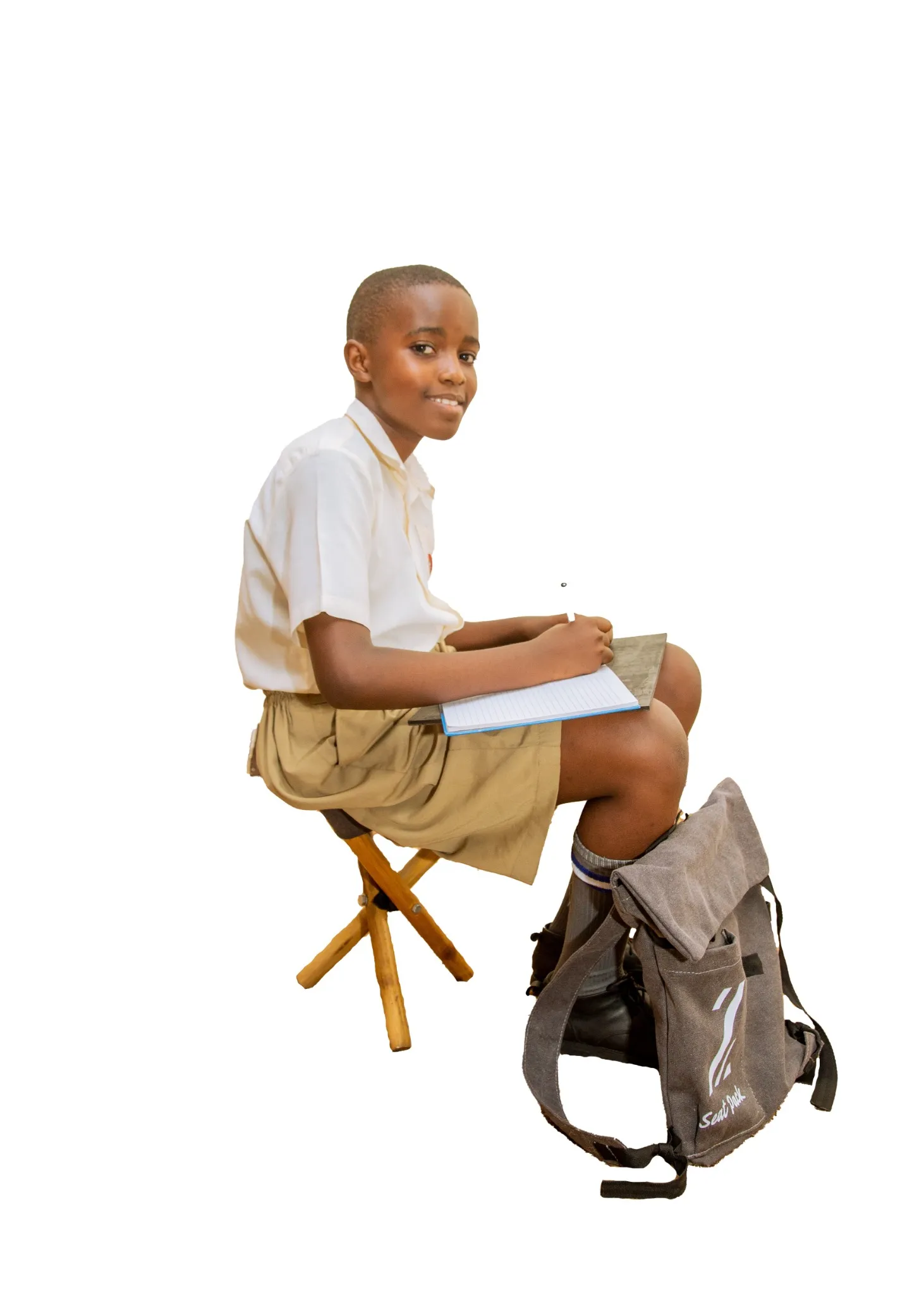 A young student in Uganda sits on the ground, smiling as they unpack books from their Zetu Seatpack, which is converted into a small desk in front of them.